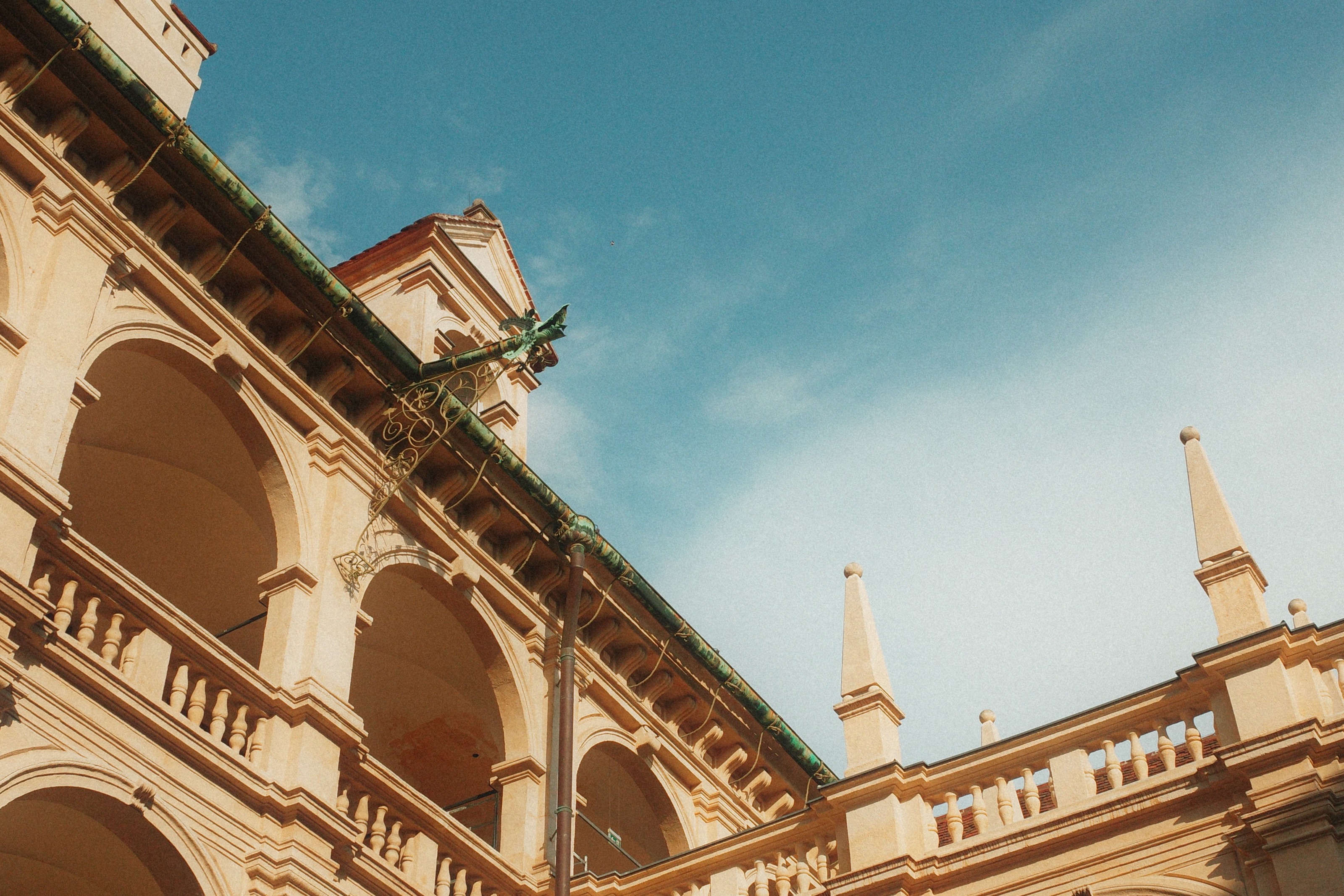 Arcaded renaissance courtyard from below, a green copper gutter running along the roofline against a blue sky