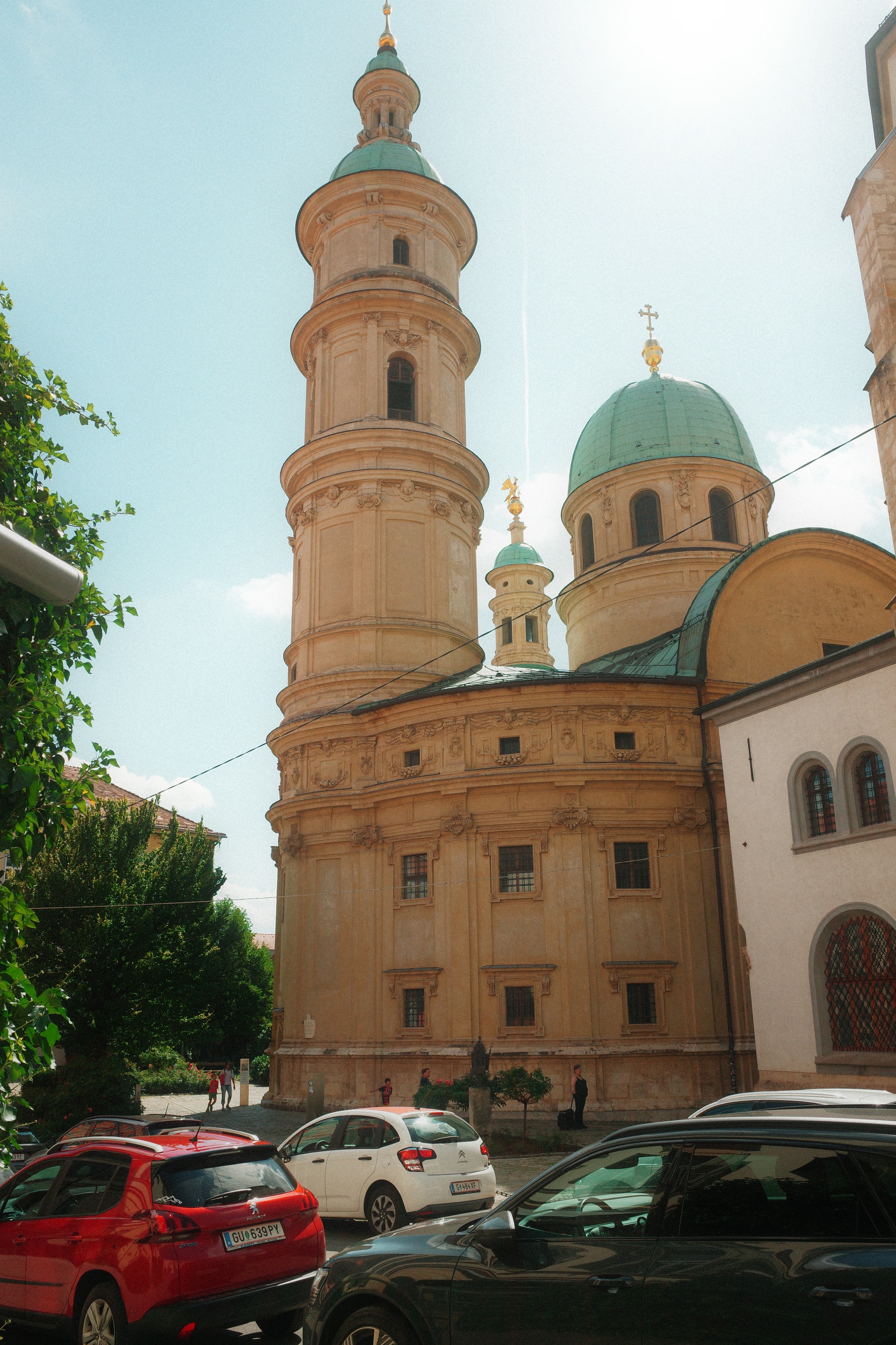 A round bell tower and green copper dome rising over a street of parked cars