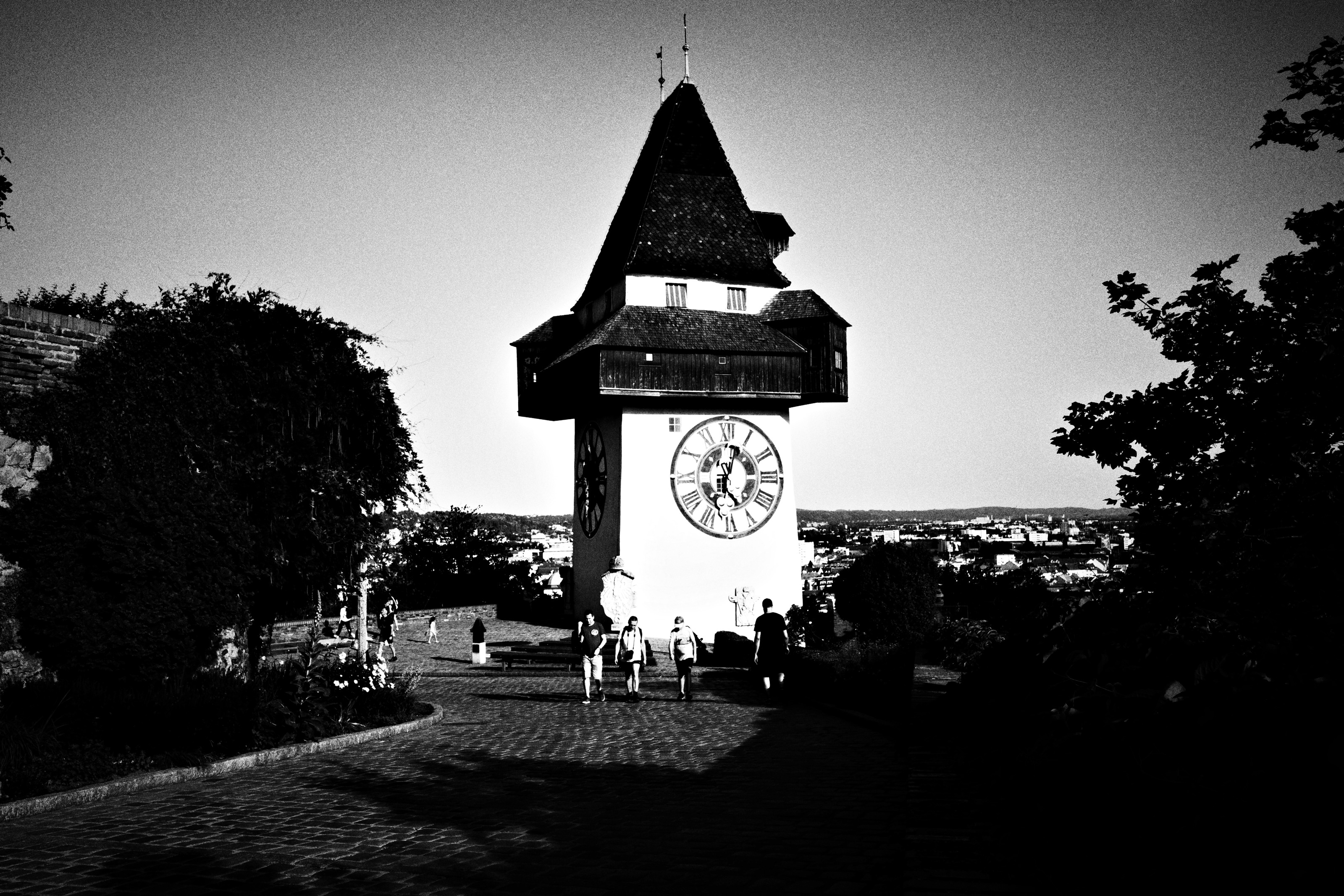 Black and white view of a clock tower on a hill, people walking a gravel path below