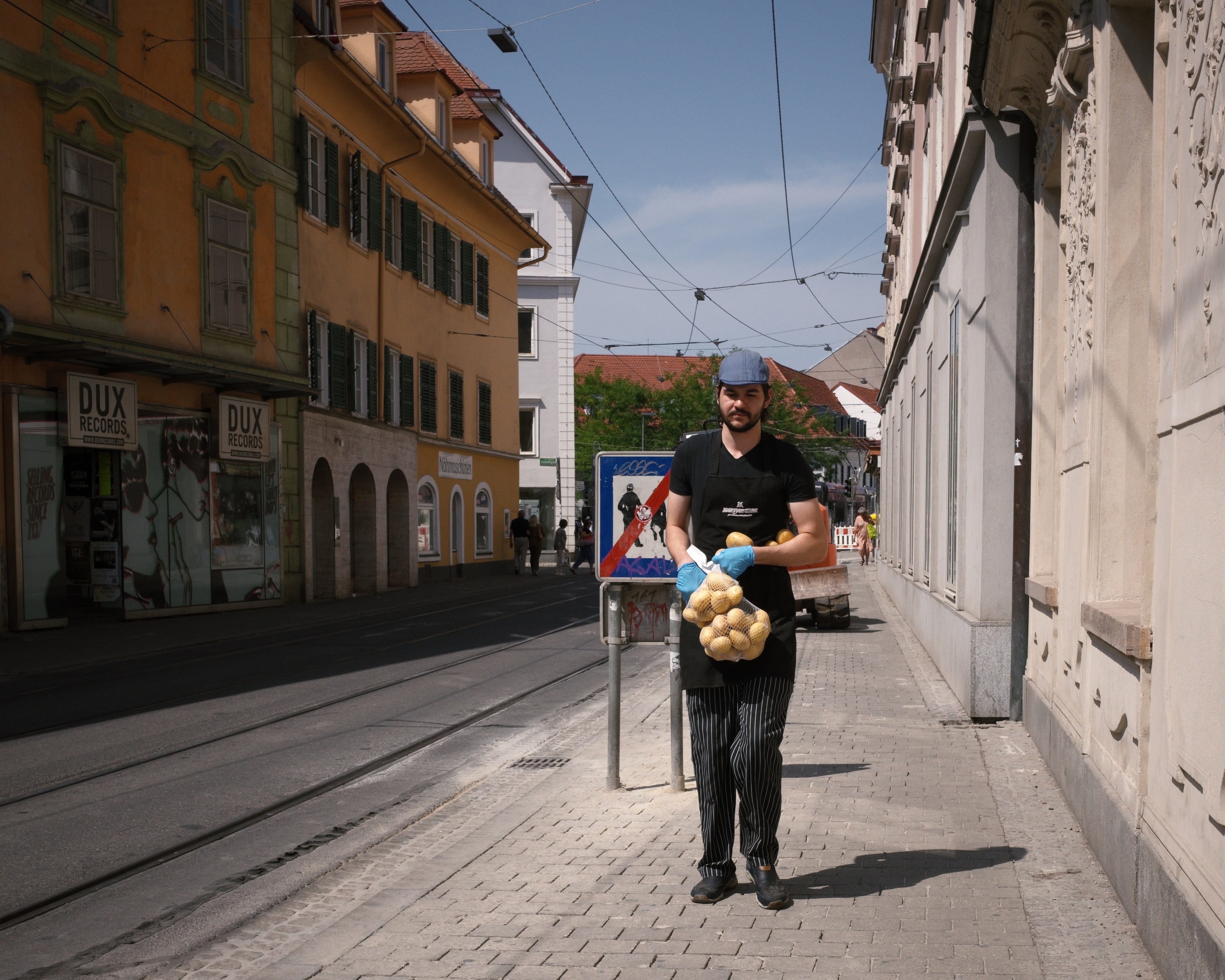 A cook in an apron carrying a full net of potatoes down an empty street at midday