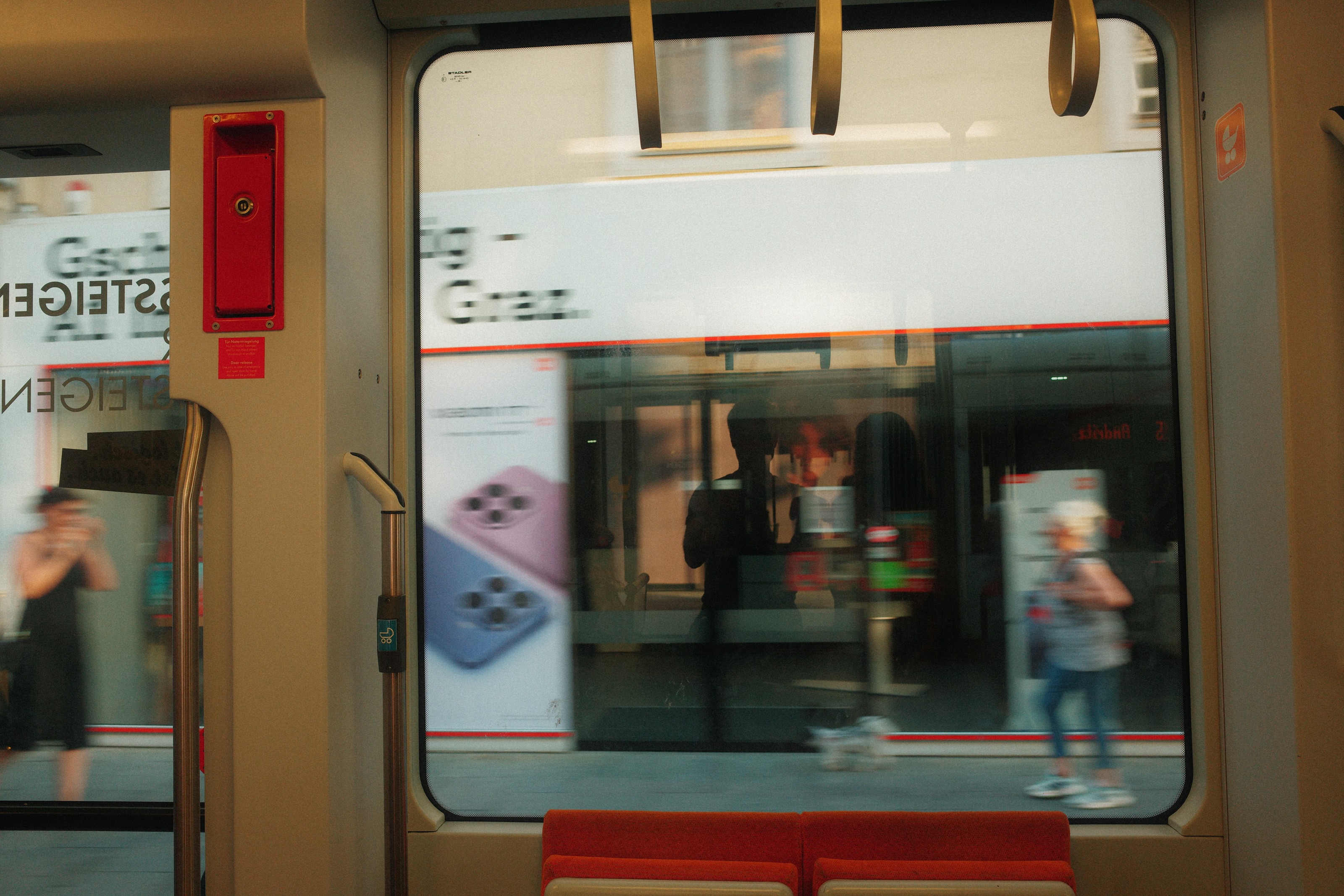 From inside a tram, the platform sliding past the window with reflections layered over it
