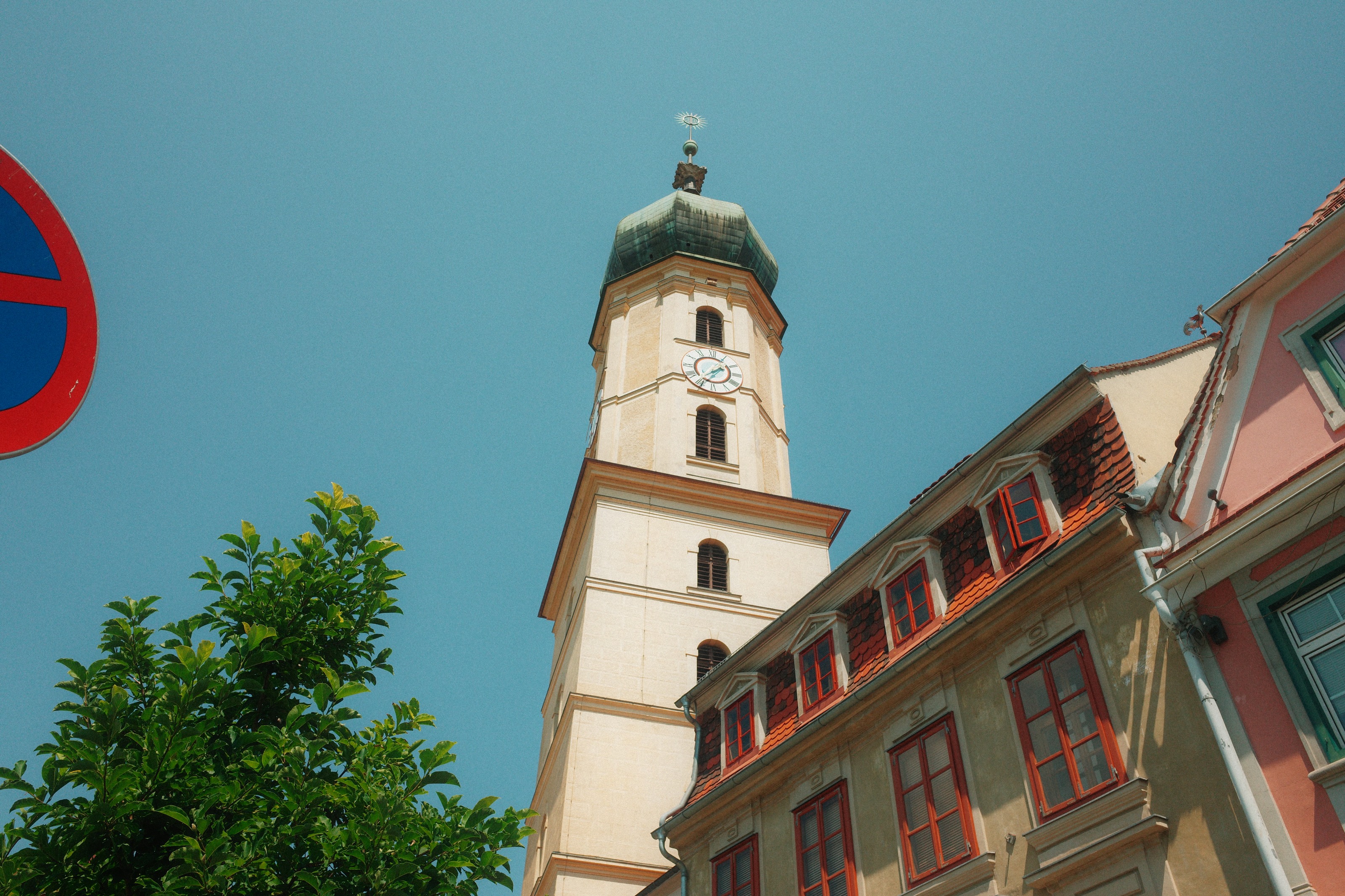 A church tower with a green dome rising behind red-shuttered rooftops